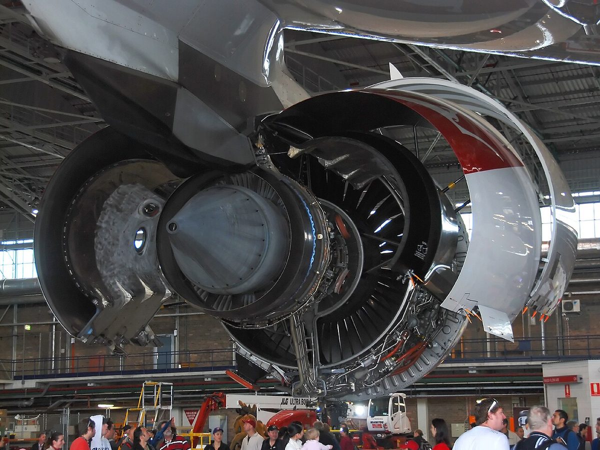 A Rolls-Royce Trent 900 engine with its cowlings open under the wing of a Qantas Airbus A380 in a hangar.