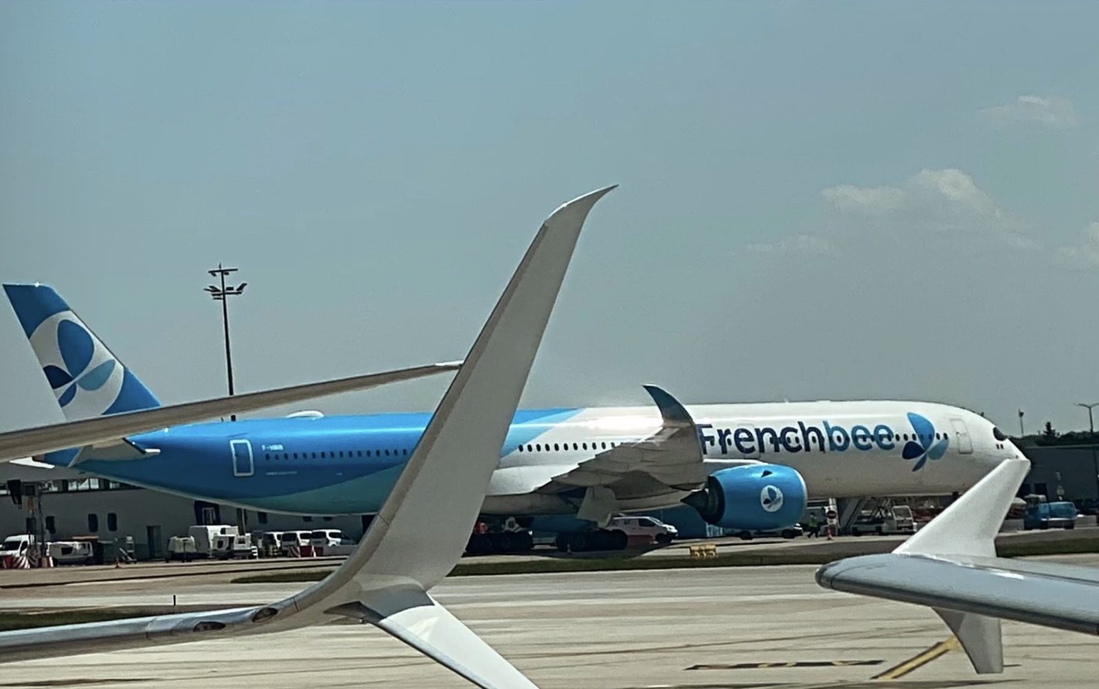 A French bee Airbus A350 on the apron, seen past the wingtip of another airliner