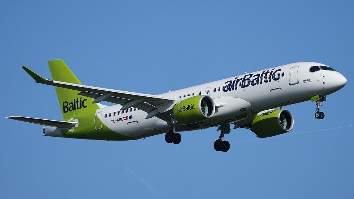 An airBaltic airliner, registration YL-ABL, on approach against a blue sky, landing gear down, white fuselage with lime-green tail and engine nacelles.