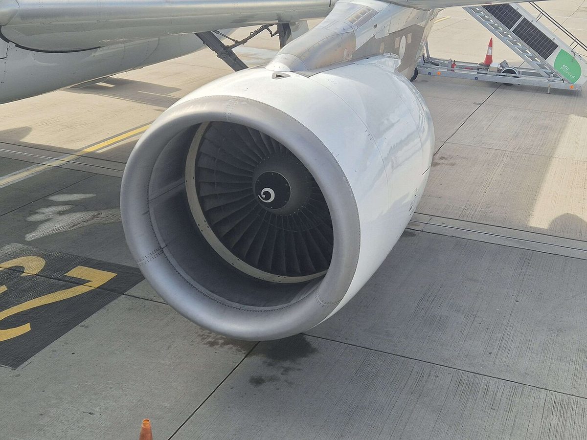 A white airliner engine under a wing seen from the front left, its fan blades and spinner visible inside the round intake.