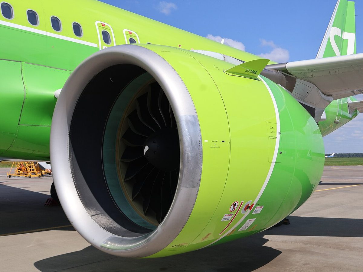 Close view of a large engine nacelle in bright green livery under an airliner wing, the fan blades visible inside the intake.