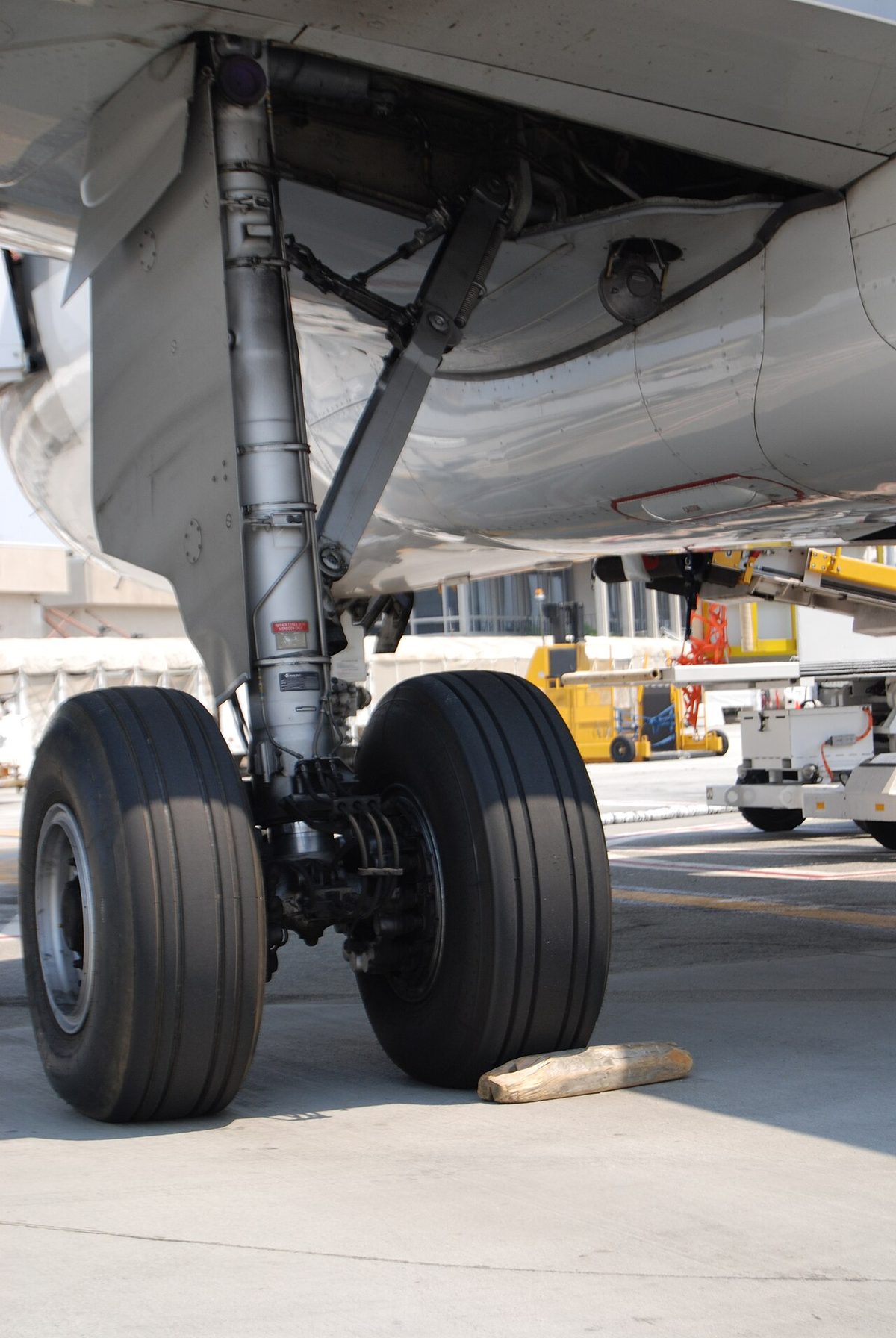 An airliner main landing gear leg on the ground: a shock strut with a bracing strut, a door panel on the leg and two large tyres.