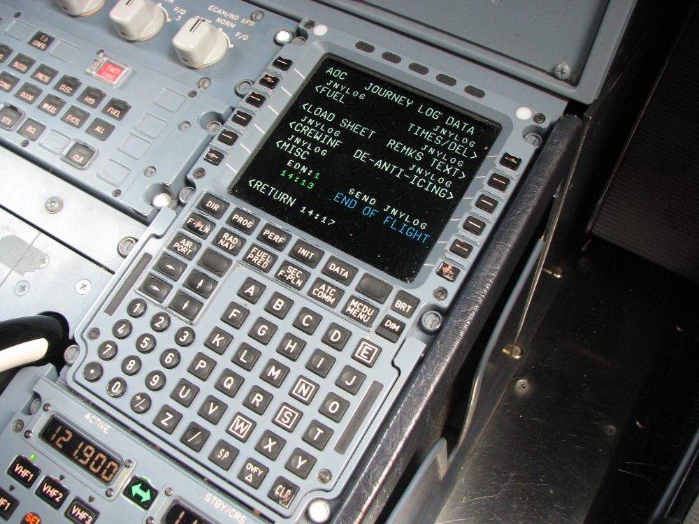 An Airbus MCDU on the flight deck pedestal: a small screen of green and white text above a full alphanumeric keyboard, with a radio management panel below.