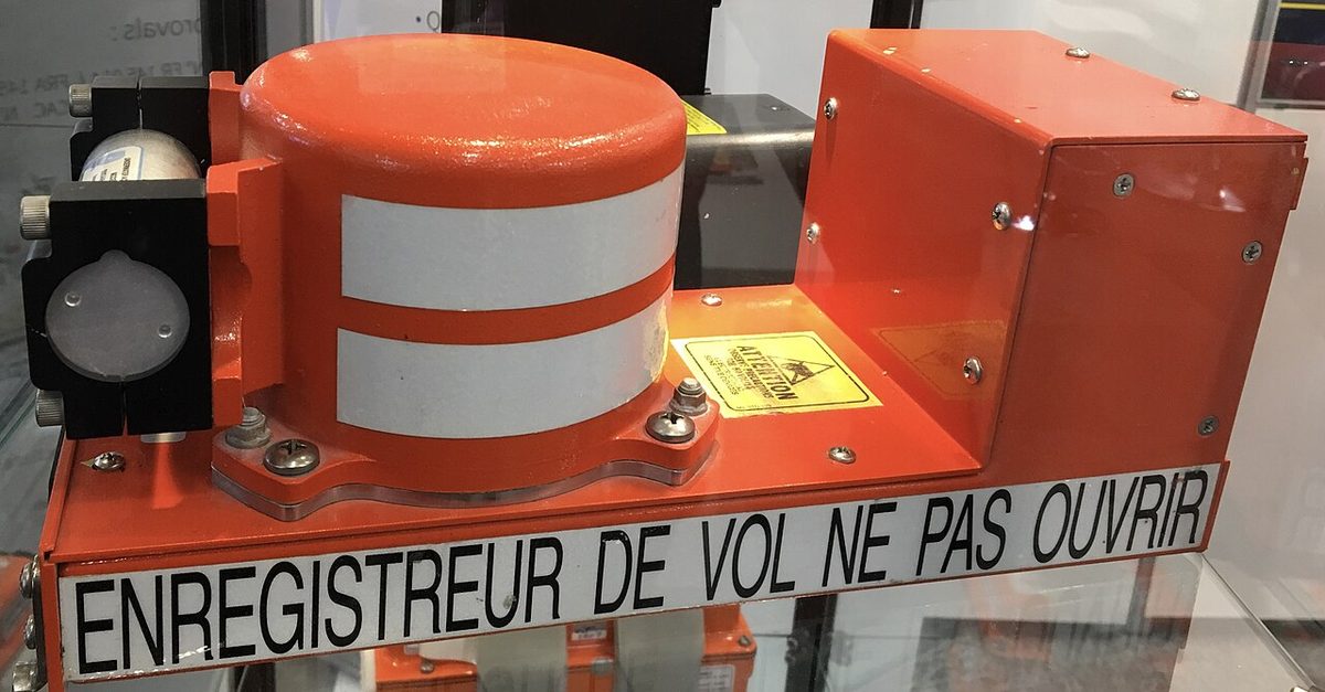 Orange flight recorder with a white-striped cylindrical unit, a small beacon on the front and a label reading ENREGISTREUR DE VOL NE PAS OUVRIR.