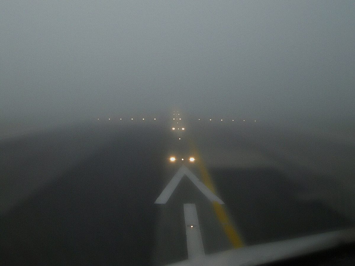 A runway at Lisbon in fog, its markings and lights fading into the grey.