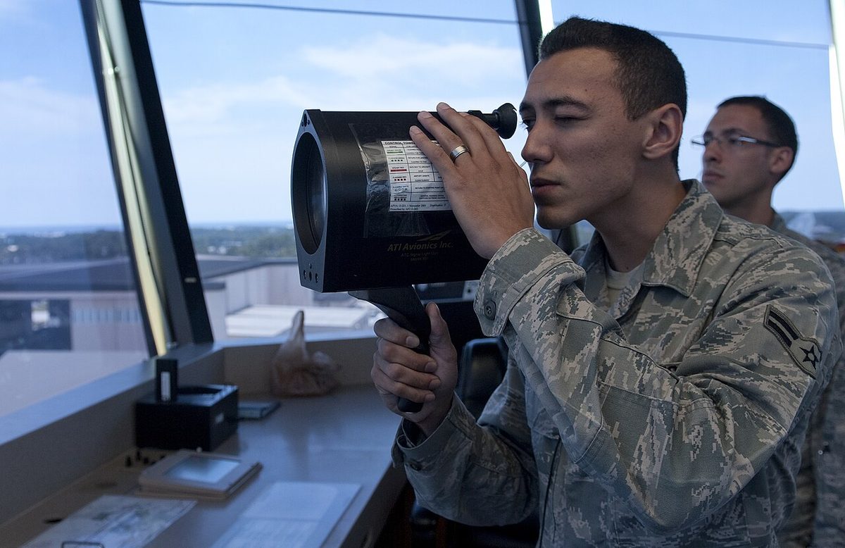 Close view of a large black signal light gun held up in both hands at a control tower window.