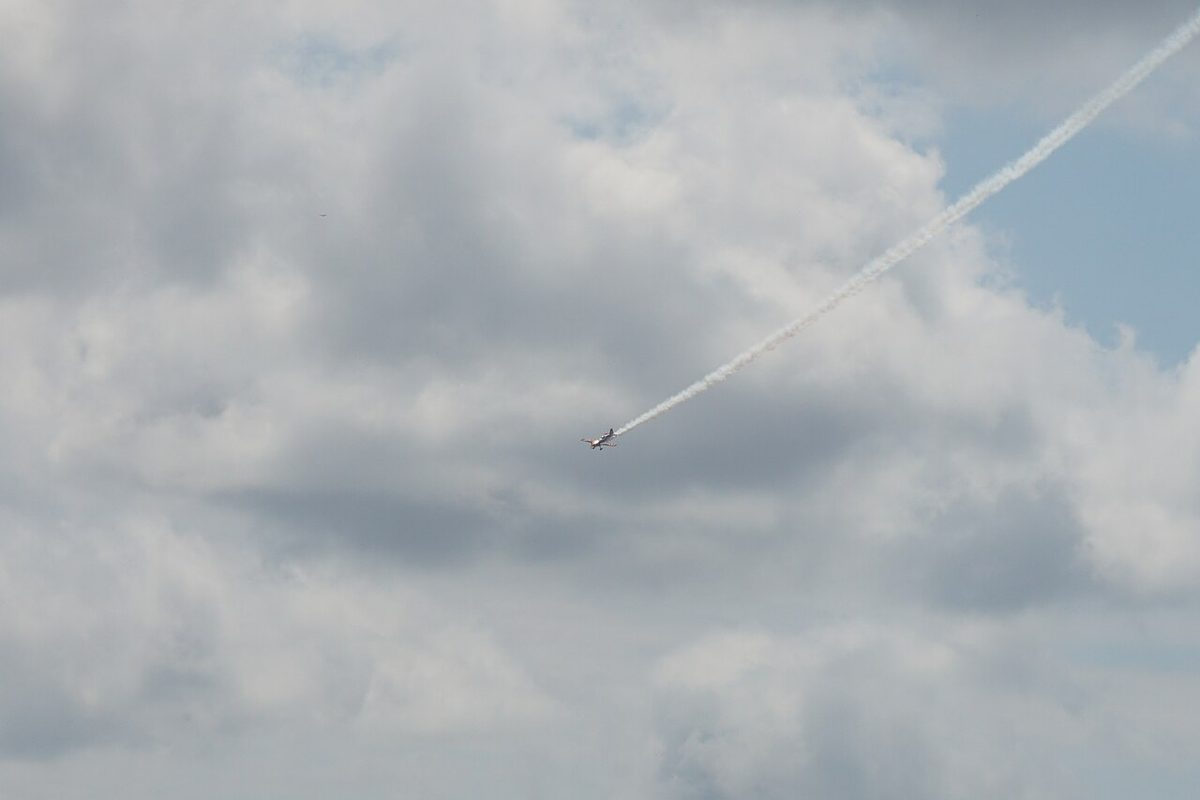 A small aerobatic aeroplane trailing display smoke against cloud at an air show.