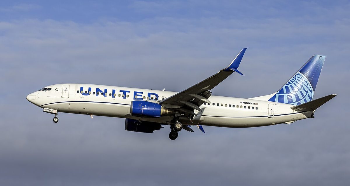 A white United Airlines Boeing 737 with a blue belly and a blue globe on its tail, landing gear down, under cloud.