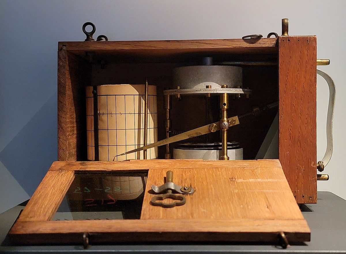 A barograph, a recording barometer in which a pen arm traces a line on a paper chart wrapped round a drum.