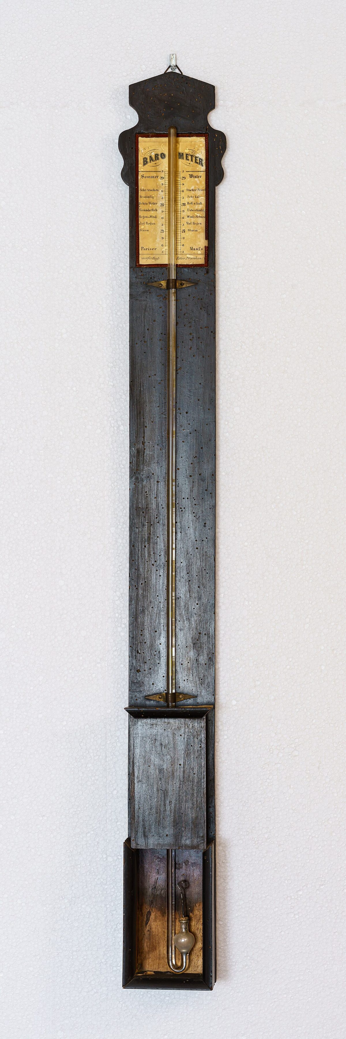 A 19th-century mercury barometer in a tall, narrow wooden case, with its scale at the top.