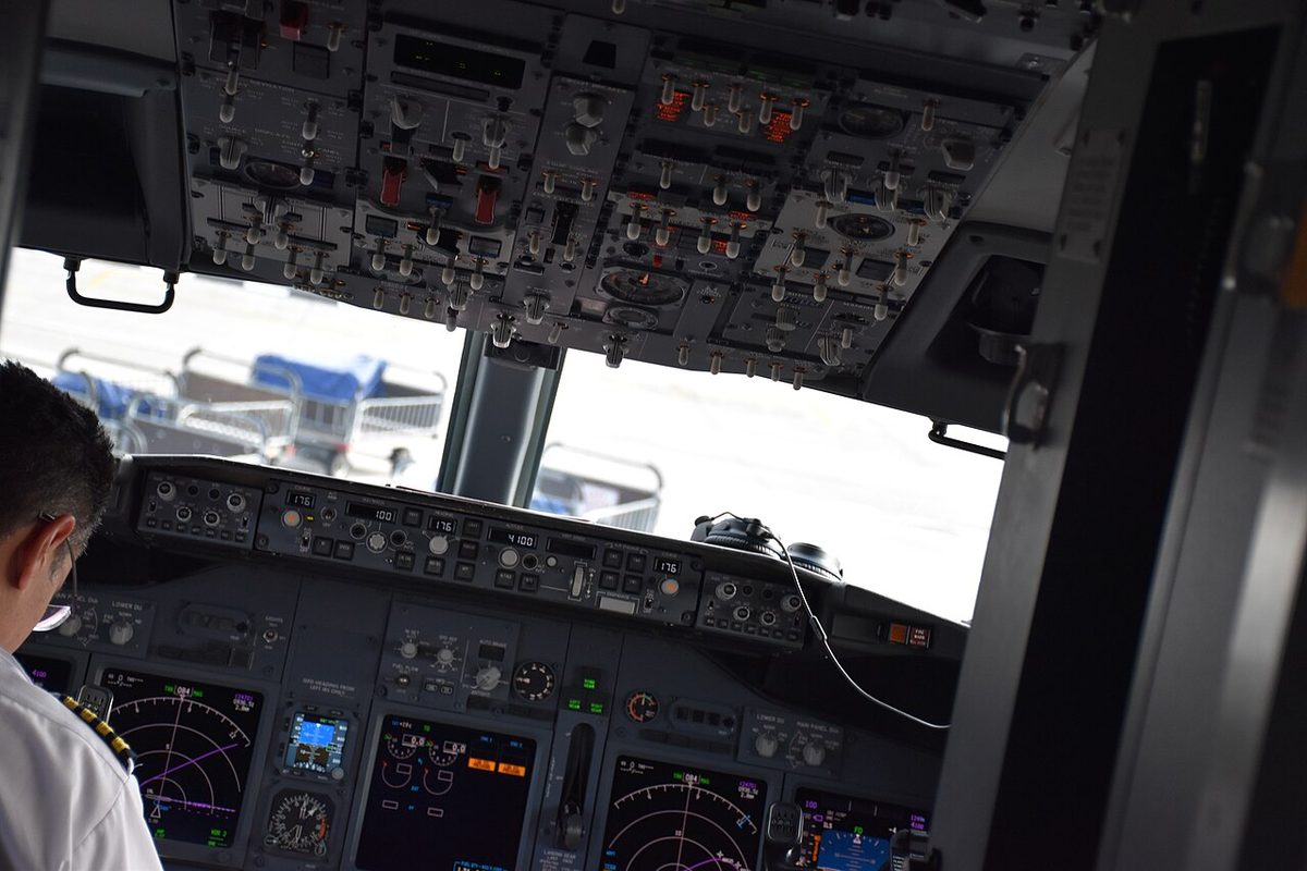 Boeing 737-800 flight deck seen from the entrance, with the captain seated at left: the overhead panel above, the mode control panel along the glareshield, and navigation, standby and engine displays below.