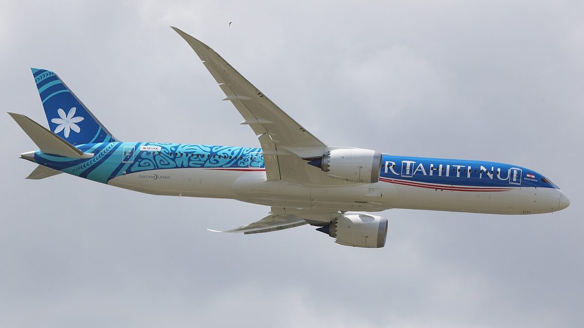 An Air Tahiti Nui Boeing 787-9 in flight under a grey sky, landing gear up, its long wings curving upward.