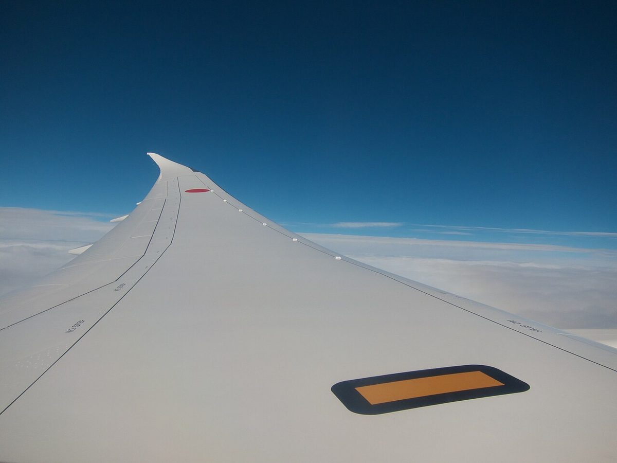 A Boeing 787 wing seen from a cabin window in flight, bending upward towards a raked wingtip.
