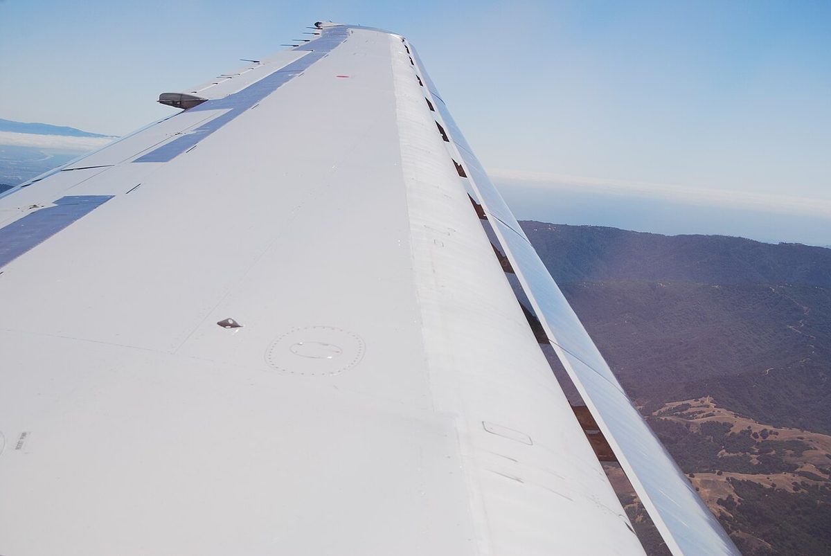View from a cabin window along an airliner wing in flight, with the slat extended ahead of the leading edge and a clear gap between slat and wing.