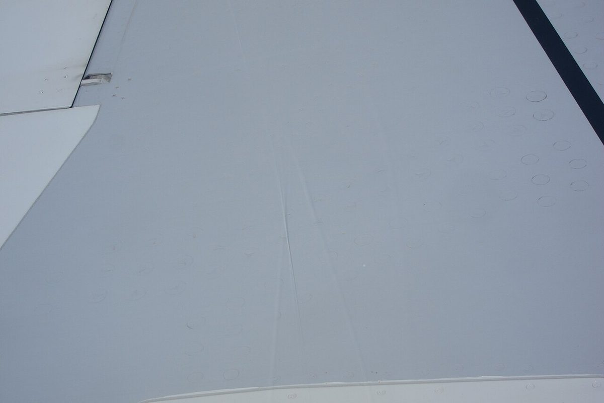 The upper surface of an airliner wing in cruise seen from a cabin window, with faint wavering lines lying across it.