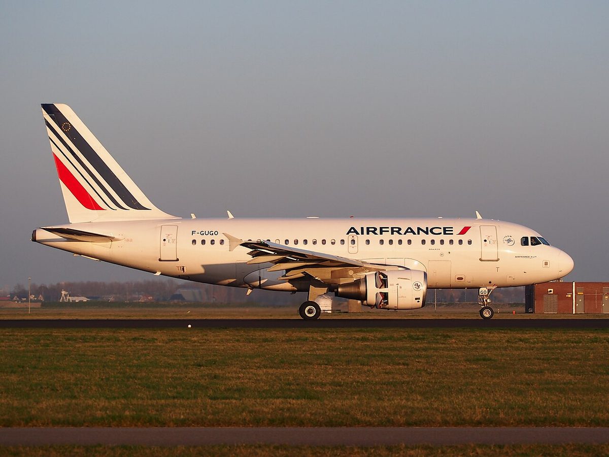 Short-bodied white twin-engined airliner with a striped tail, seen side-on on the runway in low evening sun.
