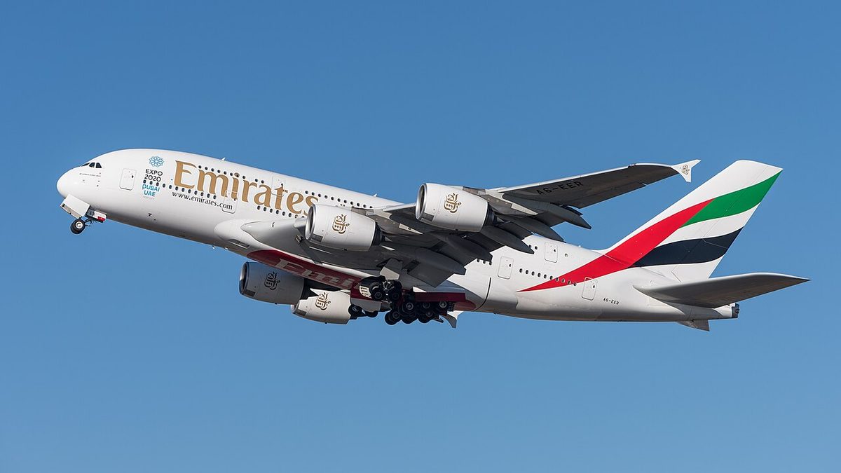 A white Emirates Airbus A380 with red, green and black tail stripes climbing away against a blue sky, gear retracting.