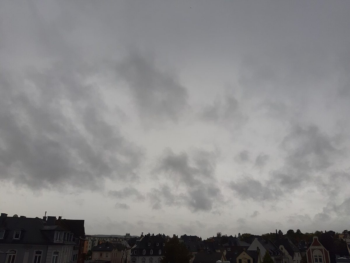 An unbroken grey overcast with darker ragged patches of cloud hanging low beneath it, above a row of rooftops.