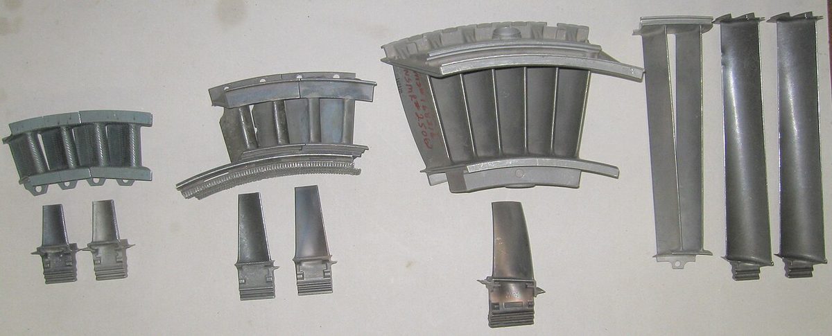 Turbine parts from a gas turbine laid out side by side: stationary nozzle vane segments and rotor blades.