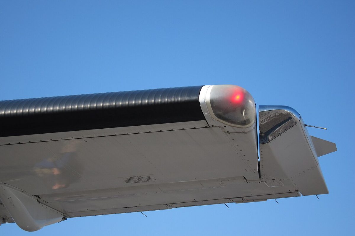 An aircraft wingtip seen from below, with a red position light and the end of the aileron extending forward into a cut-out in the wing.