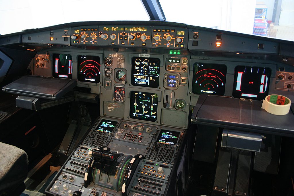 The flight deck of an Airbus A320, with display screens in front of each pilot seat and the centre pedestal between the seats.