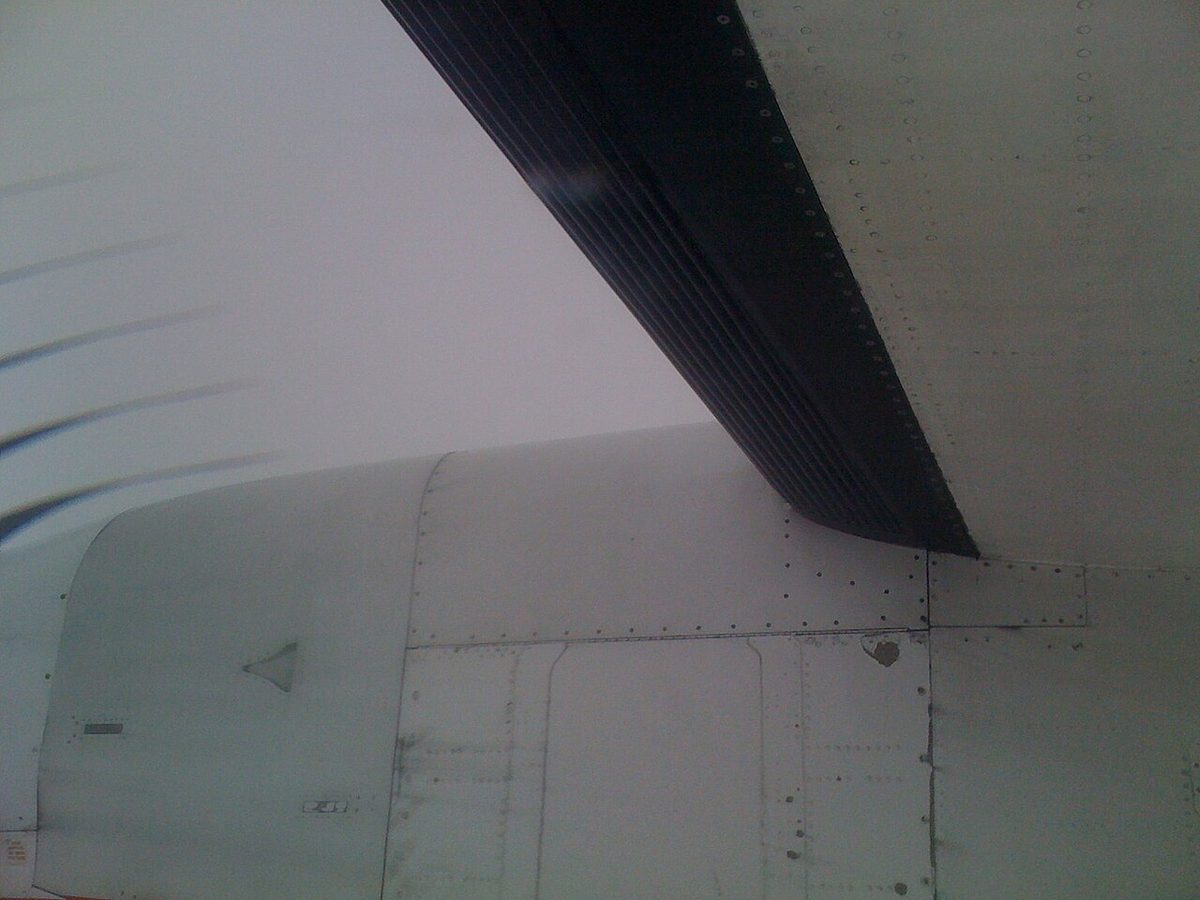 View from below of a turboprop wing leading edge covered by a black rubber boot with raised ridges running along its length.