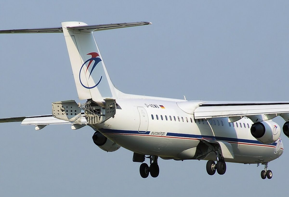 A four-engined high-wing jet on final approach with its gear down and two petal-shaped air brakes open at the tail cone beneath the rudder.