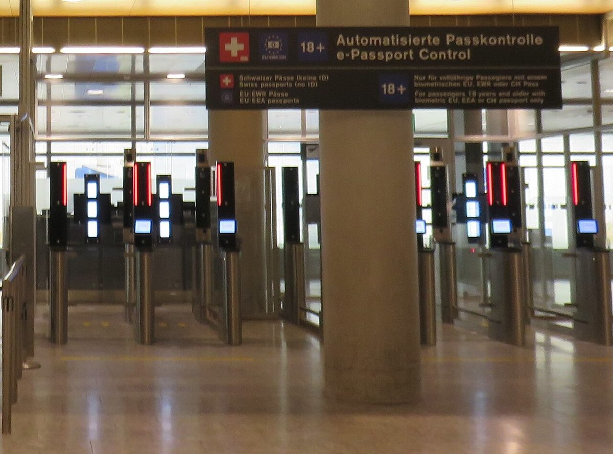 A row of automated e-passport control gates at Zurich Airport, under a sign in German and English for adults with biometric Swiss, EU or EEA passports.