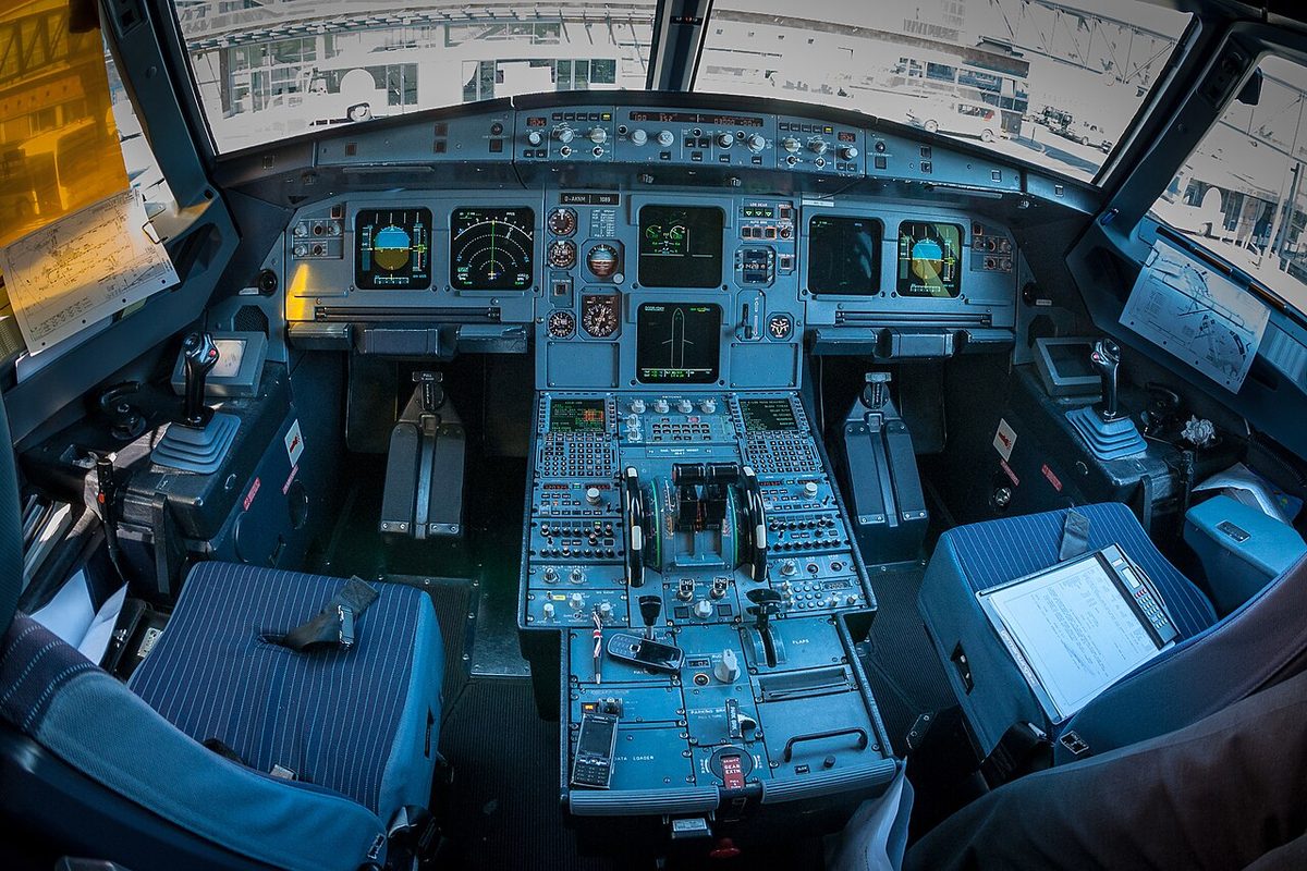 The flight deck of an Airbus A319 seen from behind the seats, with the centre pedestal between them.