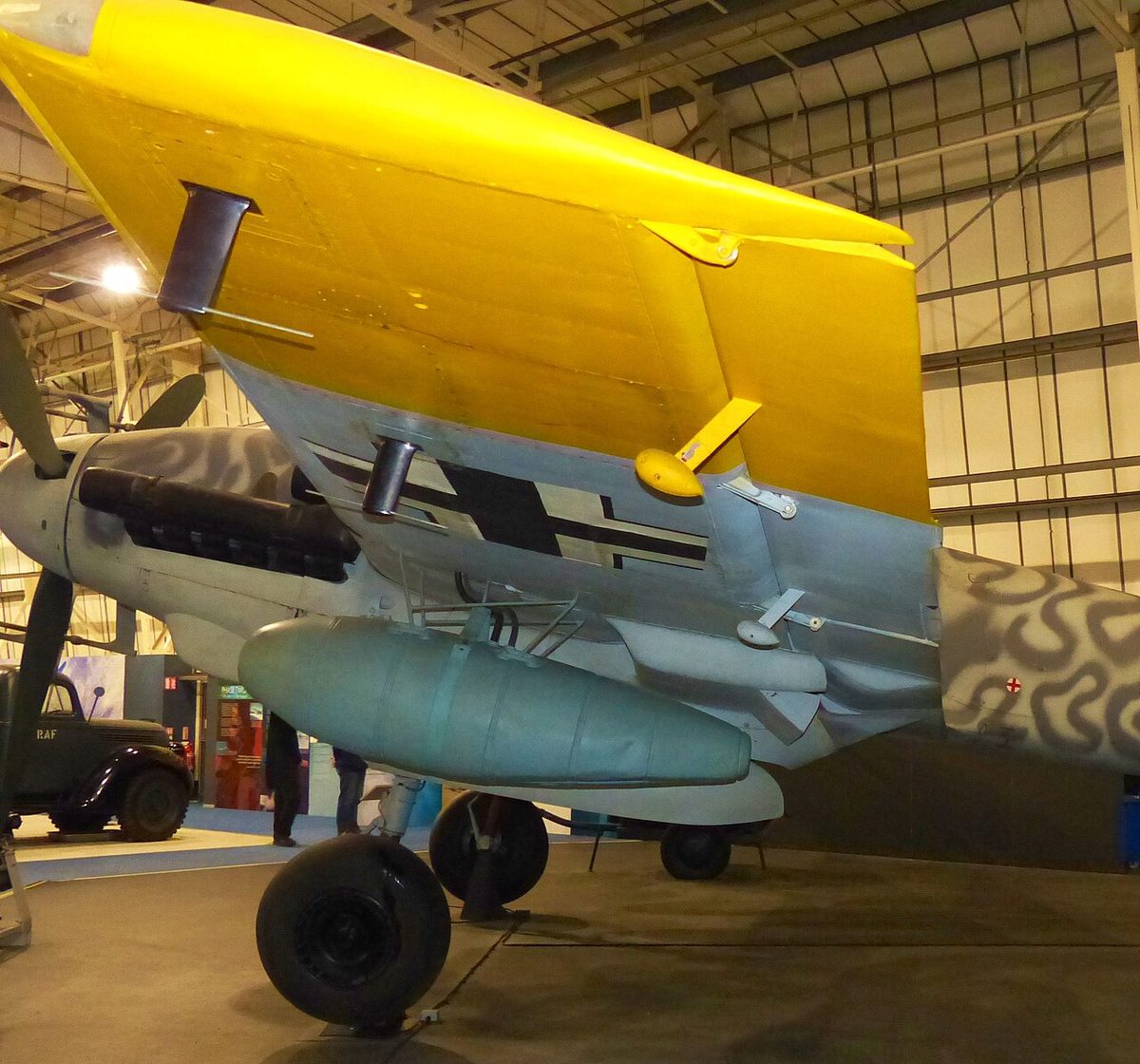 Underside of a museum aircraft's yellow-painted wing, with a small weight on an arm projecting below the aileron.