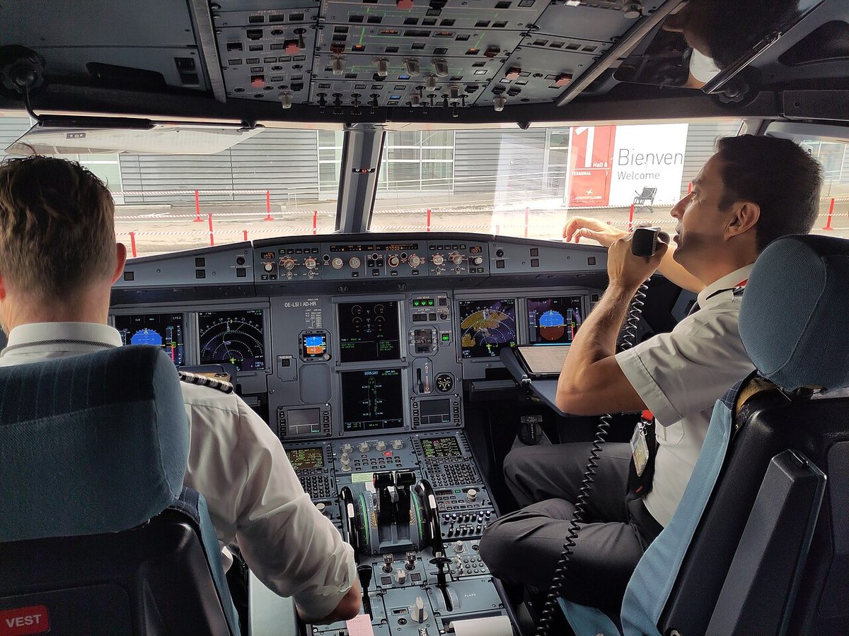 Two pilots at work on the flight deck of an Airbus A320; there is no control column in front of either seat, because each pilot flies with a side-stick on the outboard console.