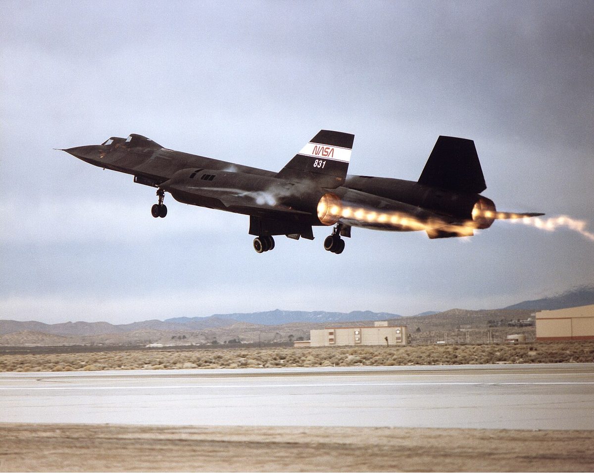 A dark jet aircraft taking off, with bright exhaust flames marked by a regular series of glowing bands.