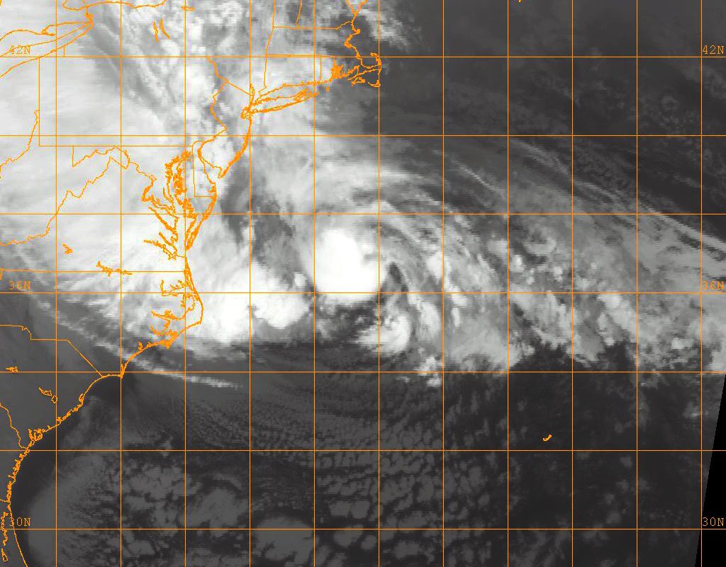 Black-and-white satellite image of a large swirl of bright white cloud off a coastline, with orange coastlines and a latitude-longitude grid over it.