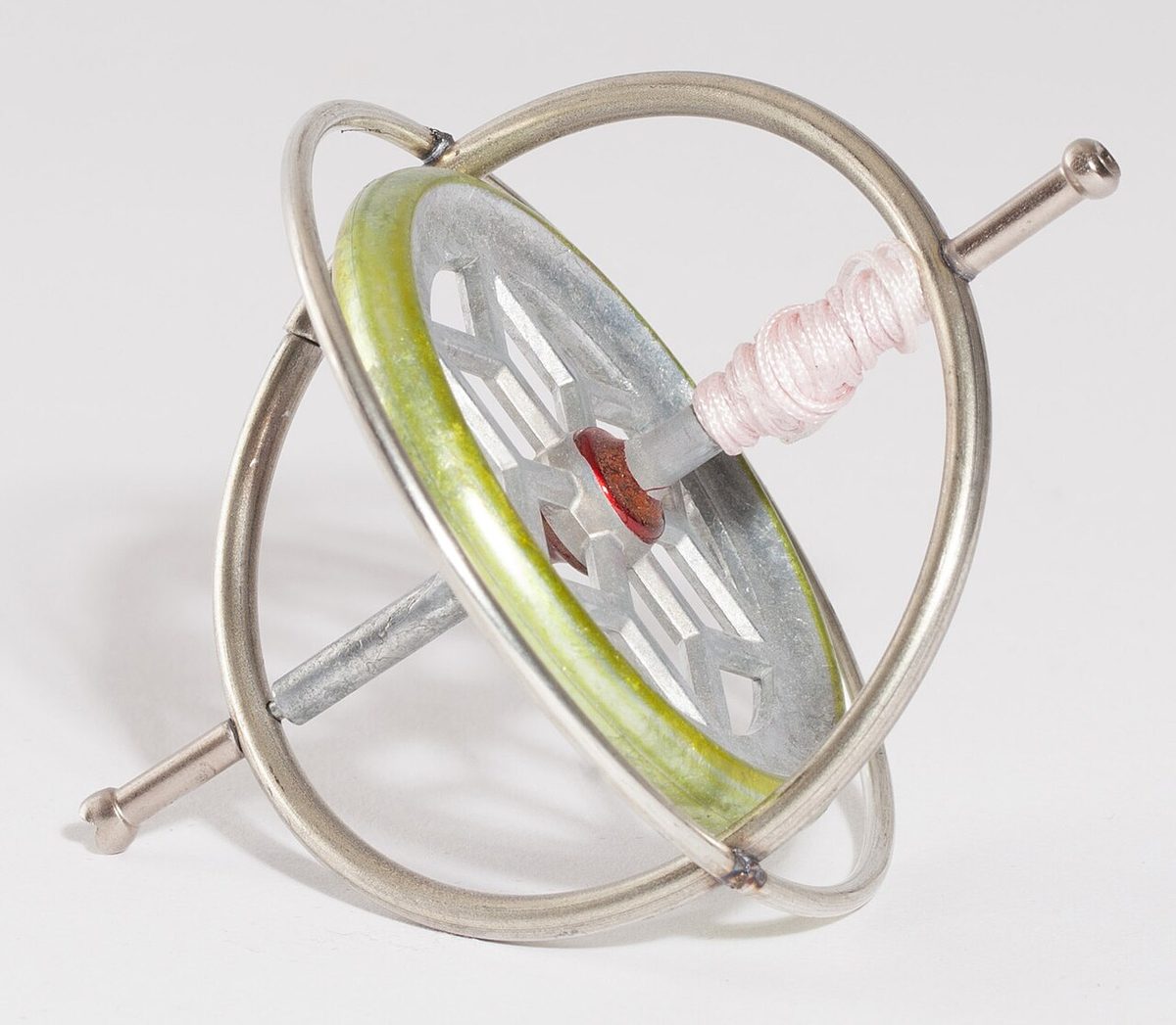 A toy gyroscope: a metal wheel with a thick rim on an axle, held in a frame of two crossed wire rings, with pink string wound round one end of the axle.