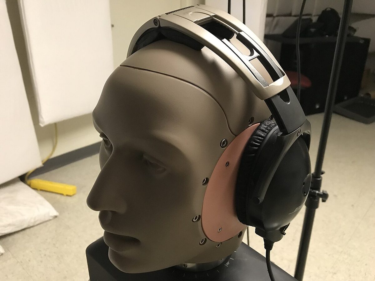 An aviation headset fitted over the artificial ears of an acoustic test fixture in a laboratory.