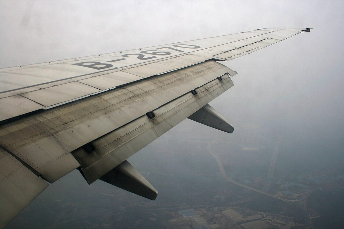 View from an airliner cabin window of the wing in flight, with the trailing-edge flap extended far behind and below the wing on its track fairings.