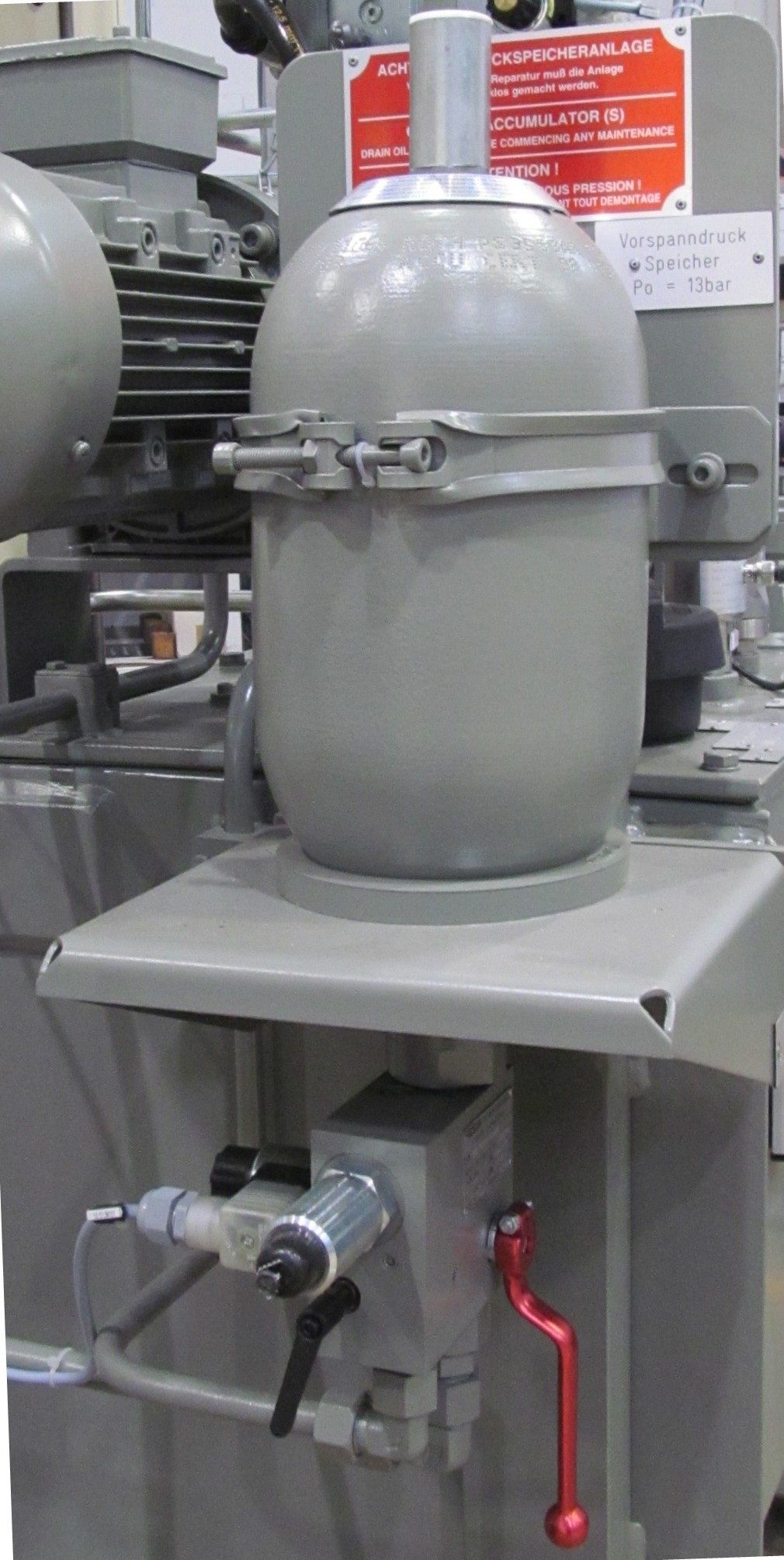 A cylindrical hydraulic accumulator with a gas charging valve at one end.
