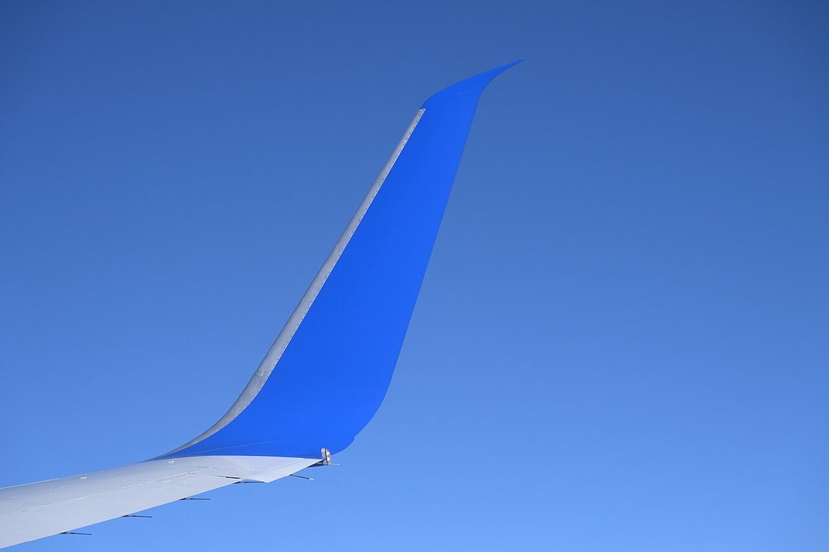 An airliner wingtip against a blue sky, curving smoothly up into a tall, swept winglet.