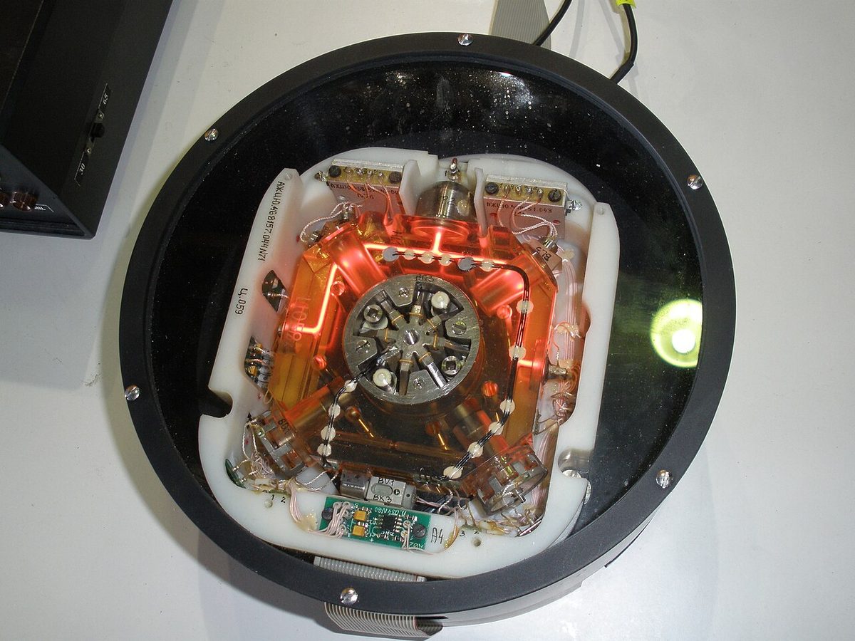 Round housing opened to show a glass block glowing orange, with light paths running round a closed loop and electronics around it.