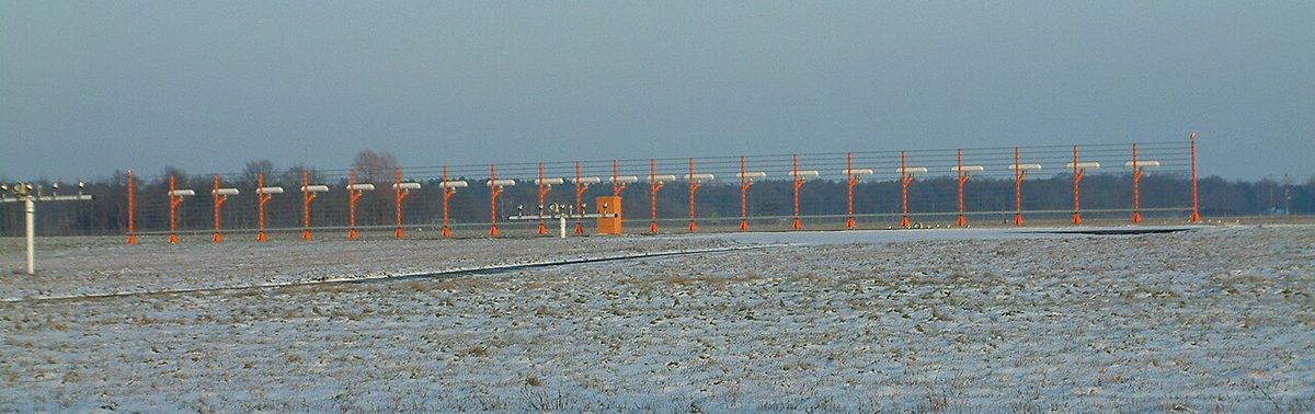An ILS localiser antenna array, a long row of identical aerials on a low frame, at an airport.