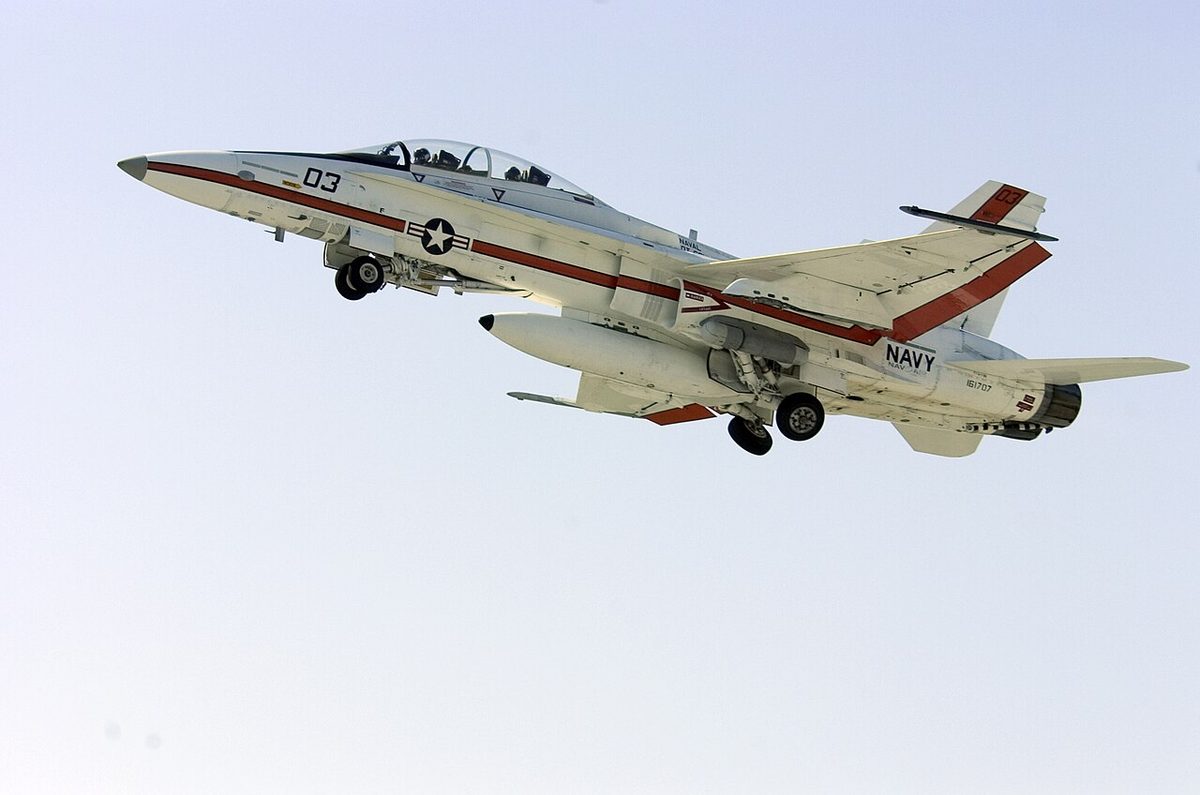 A US Navy F/A-18B Hornet climbing away just after take-off with its landing gear retracting.