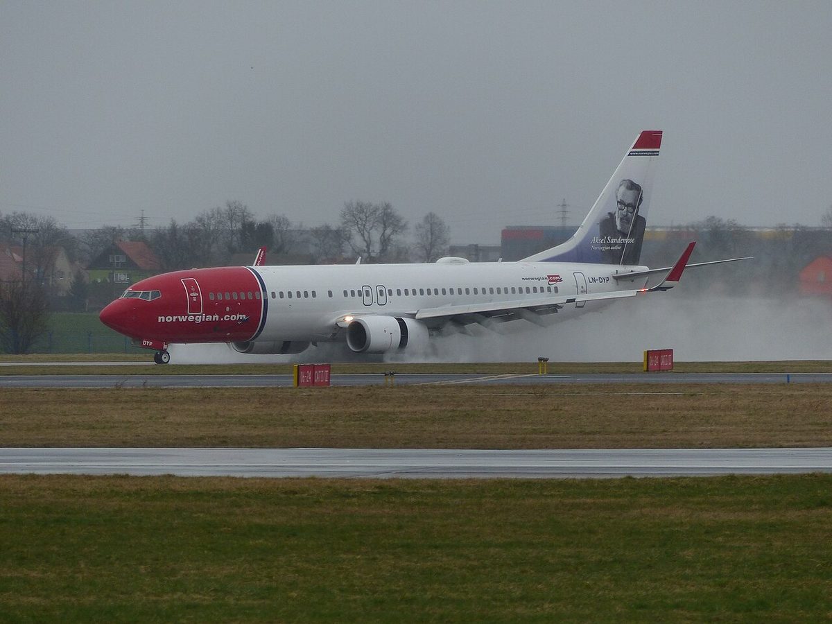 A Boeing 737 rolling along a wet runway after landing, with clouds of spray rising around its engines and wheels.