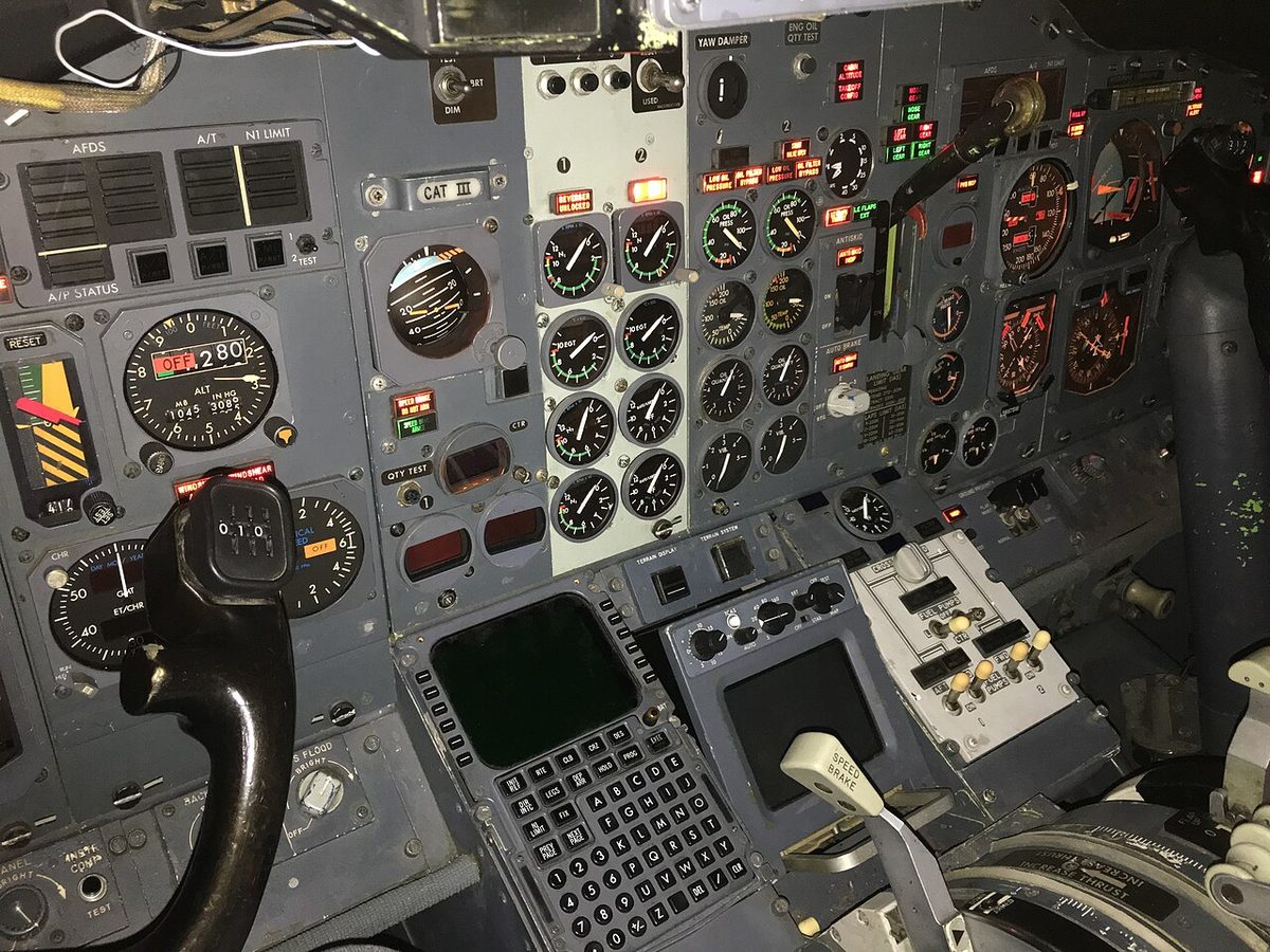 Dimly lit Boeing 737 flight deck with round-dial instruments; at the bottom centre is the FMS control display unit, its screen blank, with line select keys on both sides, function keys such as INIT REF, LEGS, PROG and EXEC, and a keypad.