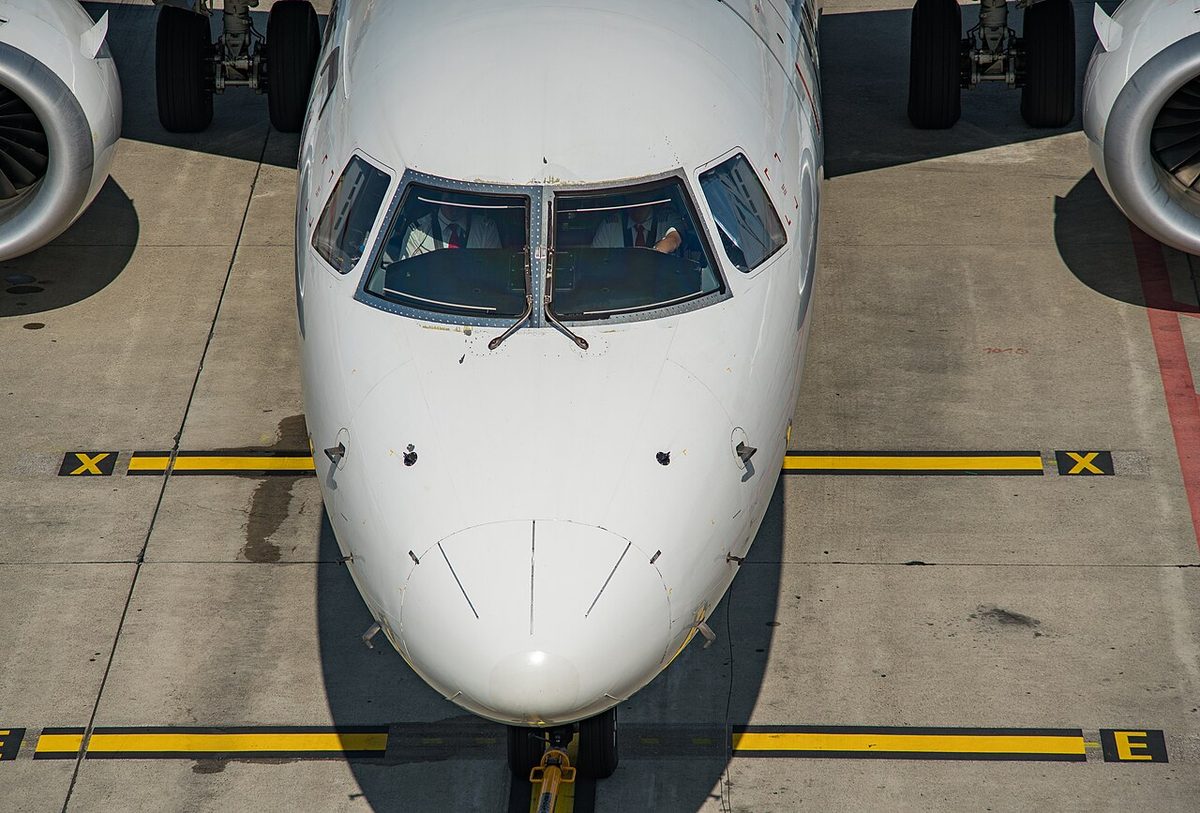 The nose of a twin-engined regional jet on its stand, with its two pilots visible through the flight deck windows.