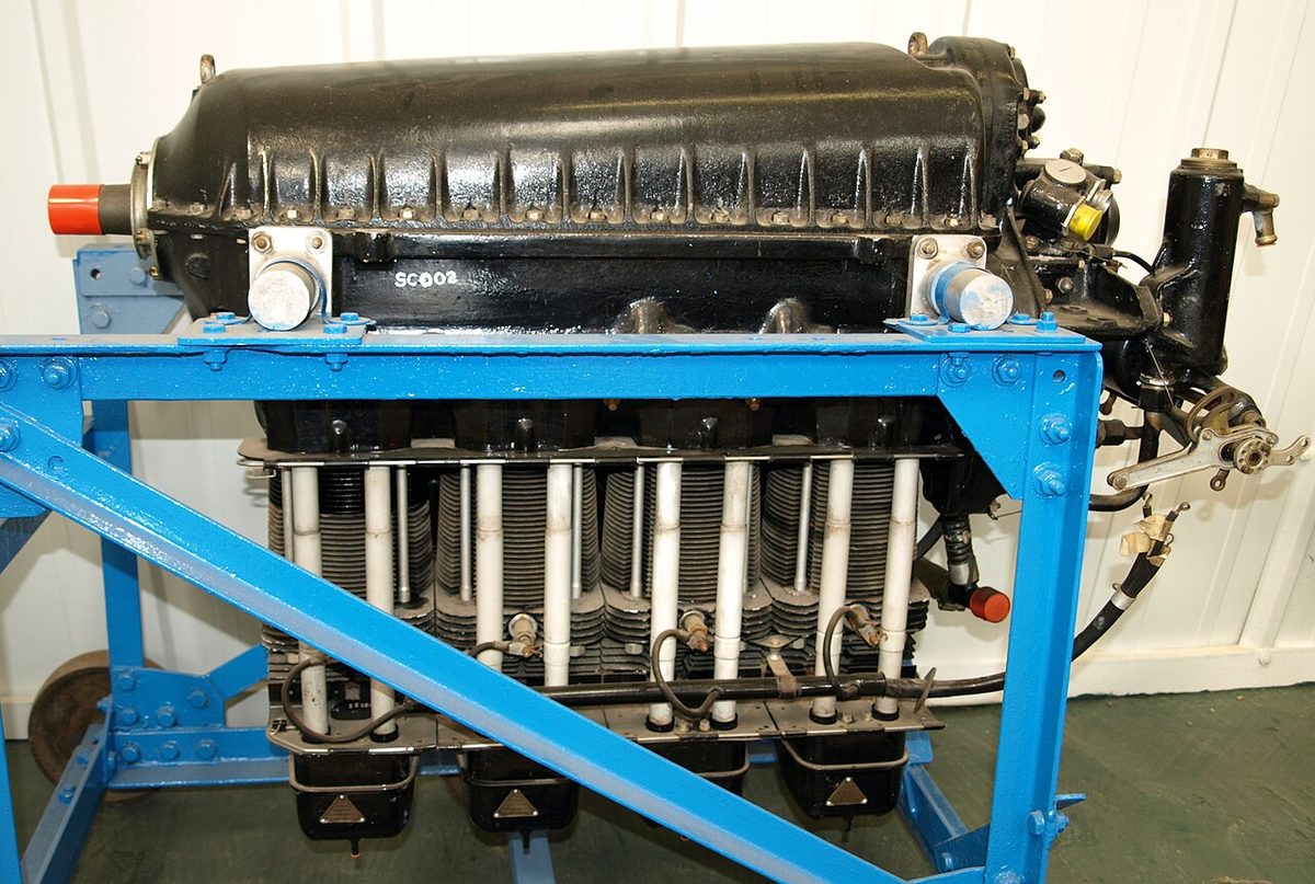 A black aircraft piston engine on a blue display stand, four finned cylinders in a row hanging below the crankcase.