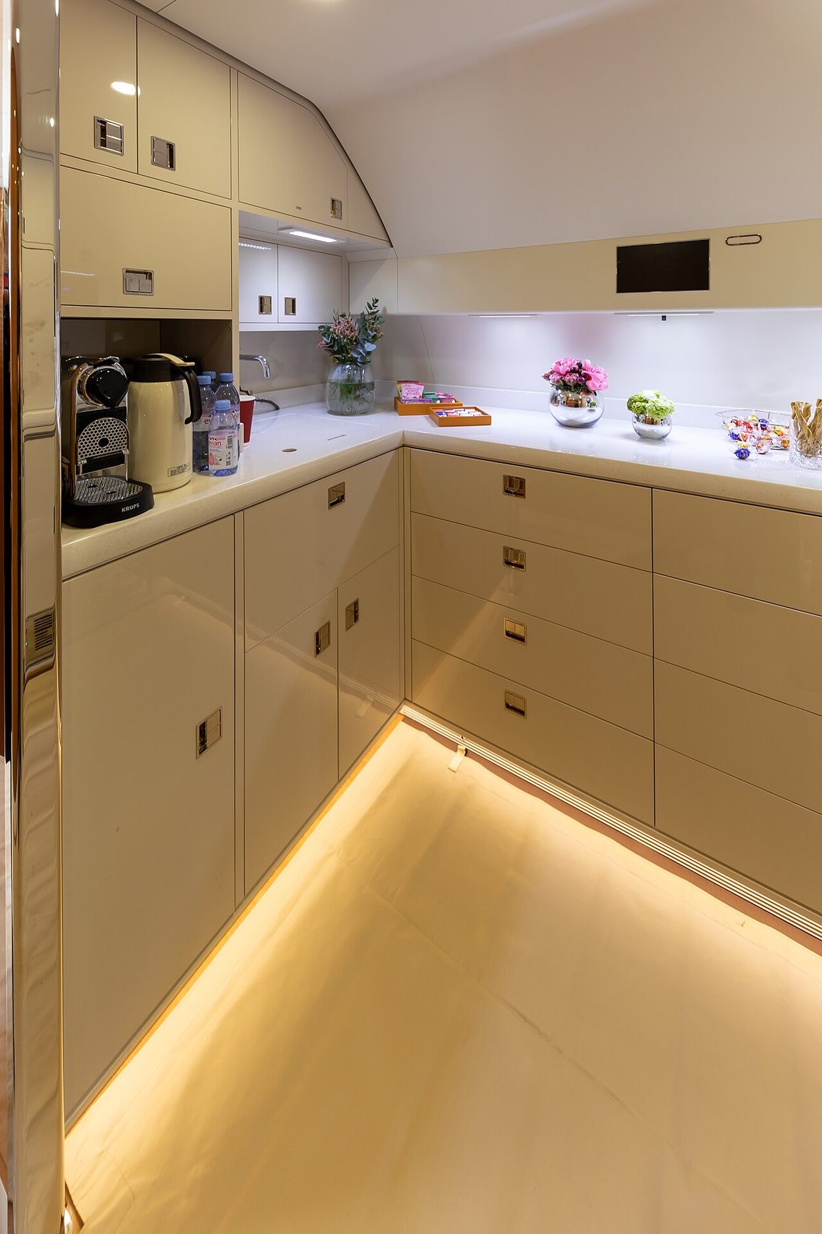 An aircraft galley with stowage cabinets, a sink and a coffee machine on the worktop.