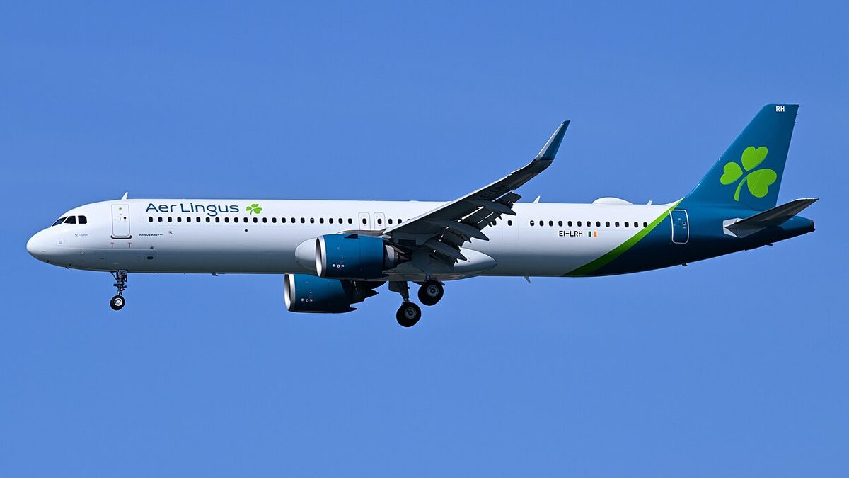 A twin-engined airliner in Aer Lingus colours flying against a clear blue sky with its landing gear down.