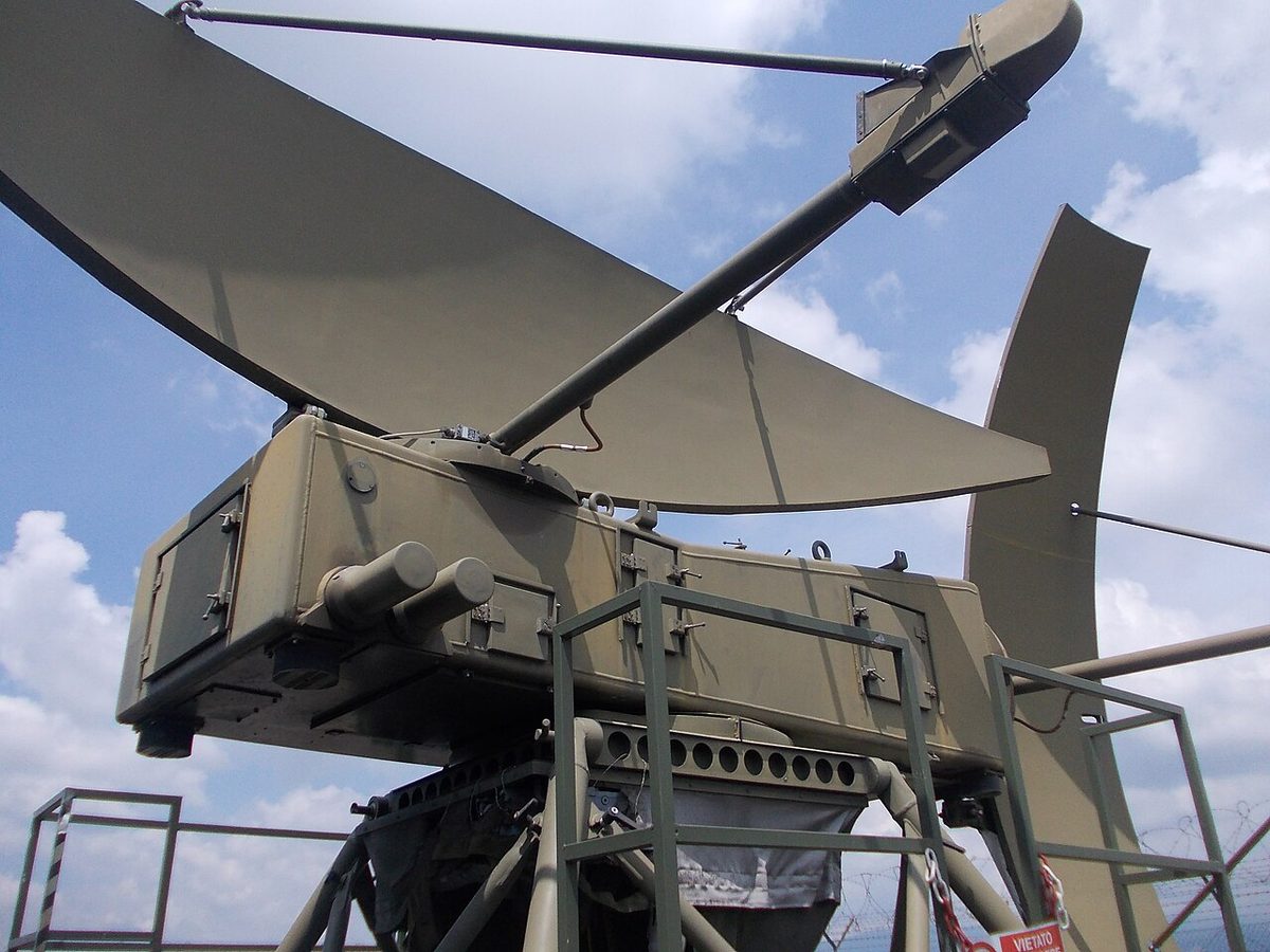 Close view of the olive-green antennas of a precision approach radar: a wide curved reflector lying horizontally and a tall curved reflector standing upright beside it, on a box-shaped mount.