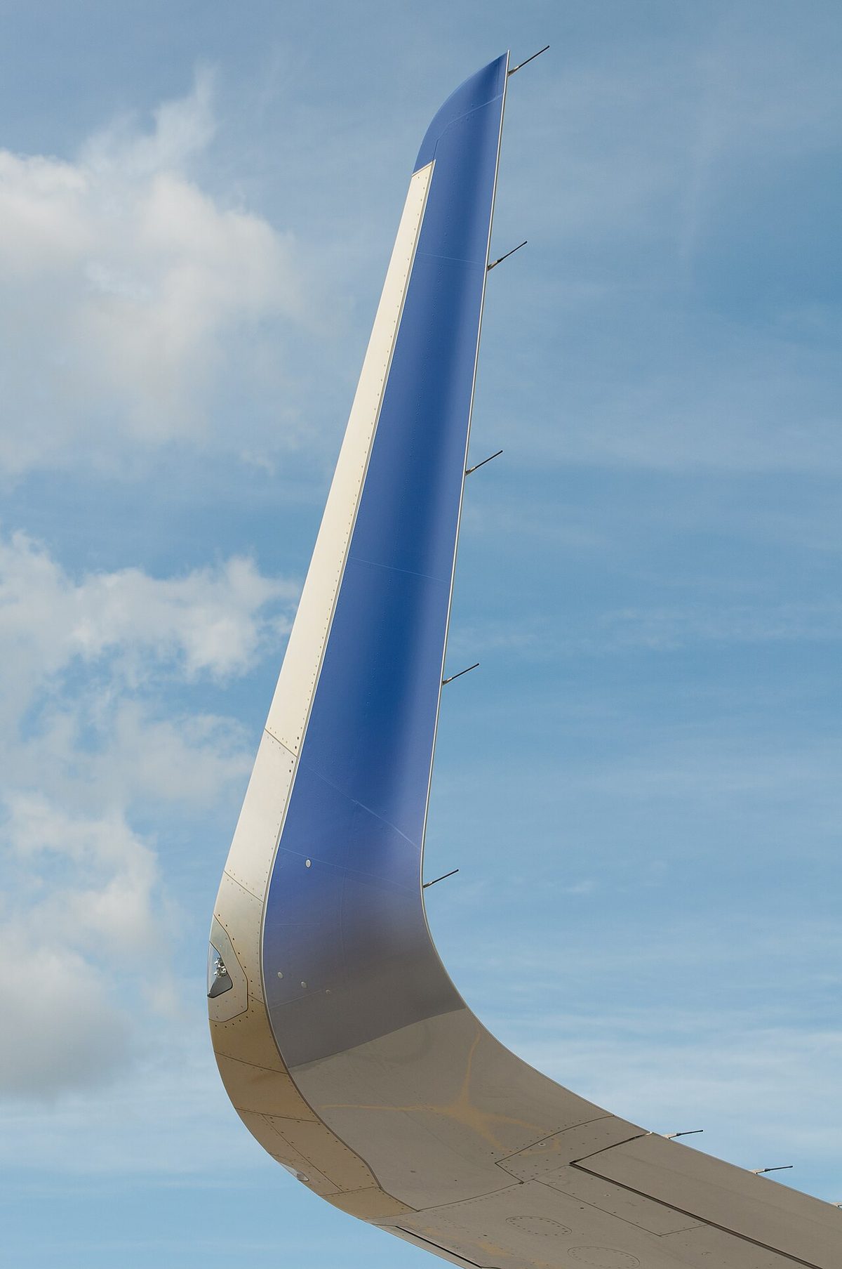 Close view of a blue and grey upswept wingtip device curving up from the end of an airliner wing against a cloudy sky.