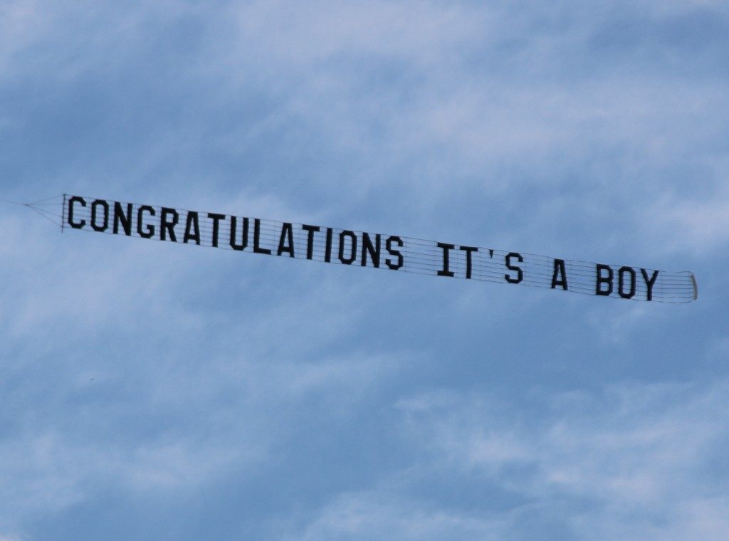 A long banner reading CONGRATULATIONS IT'S A BOY towed across a cloudy sky, the towing aircraft out of the picture.